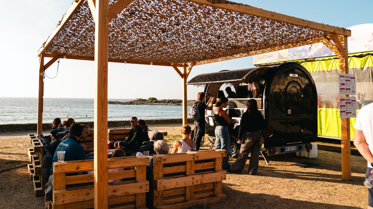 Foodtrailer aan het strand, gasten aan tafel onder de pergola